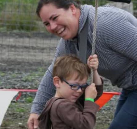 Image of Kim Caughey, playing outside with her son on a rope swing.